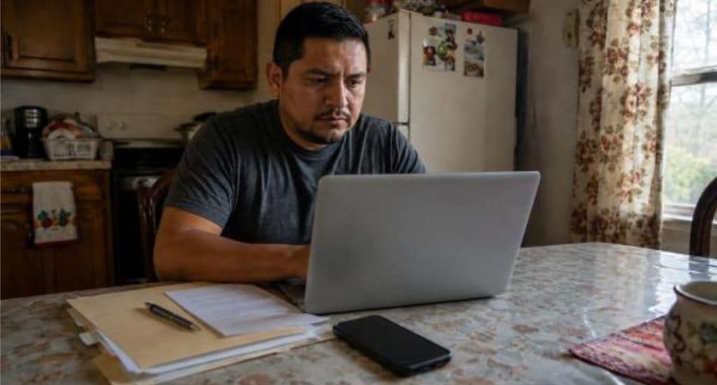 Persona hispana en Indiana buscando ayuda legal de inmigración con documentos y laptop