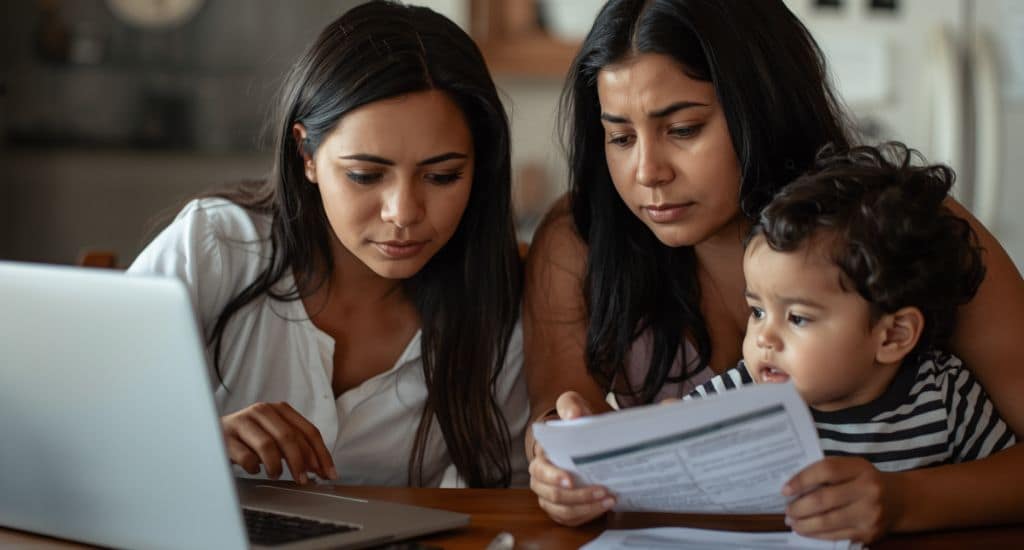 Familia hispana en Texas revisando documentos de Medicaid y seguro médico en una laptop desde casa.