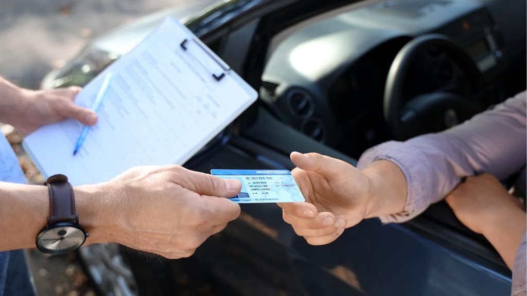 Persona sosteniendo su licencia de conducir recién obtenida frente al volante de un auto en Estados Unidos.